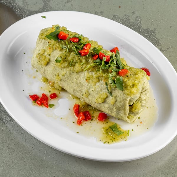 A Raging Burrito smothered in green salsa, topped with cilantro and diced red peppers on a white plate.