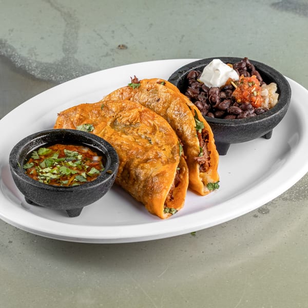 Three Raging Burrito birria tacos with a side of black beans and salsa on a white plate.