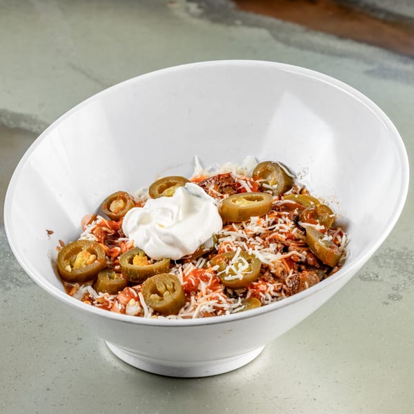 A white bowl filled with Raging Burrito's Mexican food, topped with sour cream, jalapeños, and cheese.