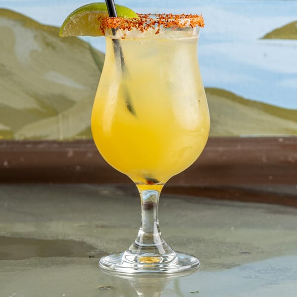 A Raging Burrito margarita with a chili-lime rim and a lime wedge, against a painted mural.