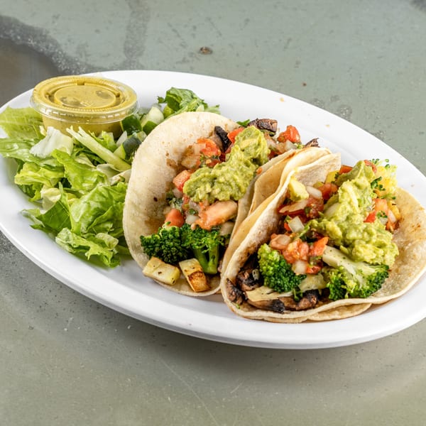 Two Raging Burrito tacos filled with vegetables and guacamole, served with a side salad and dressing.