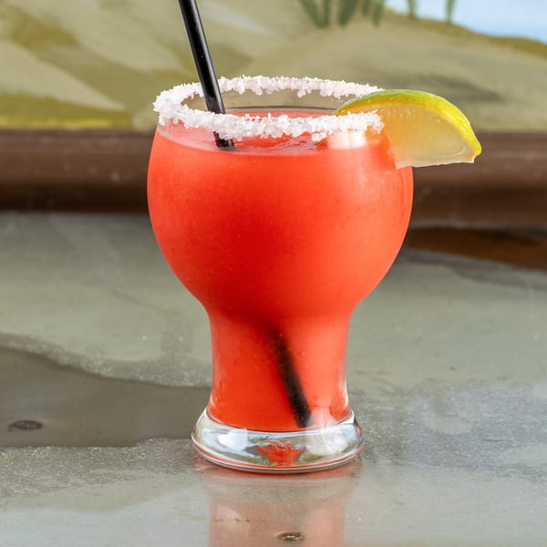A vibrant red Raging Burrito frozen margarita with a salted rim, lime wedge, and black straw.