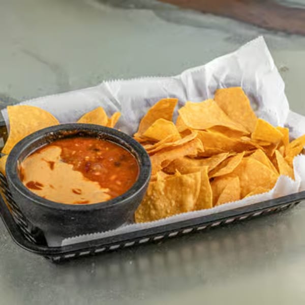A black basket of Raging Burrito tortilla chips with a side of queso and salsa.