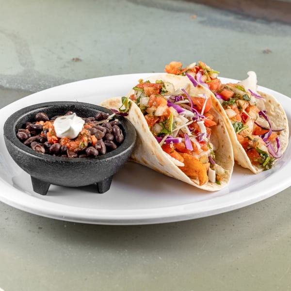 Three Raging Burrito tacos with salsa, cabbage, and black beans in a molcajete.